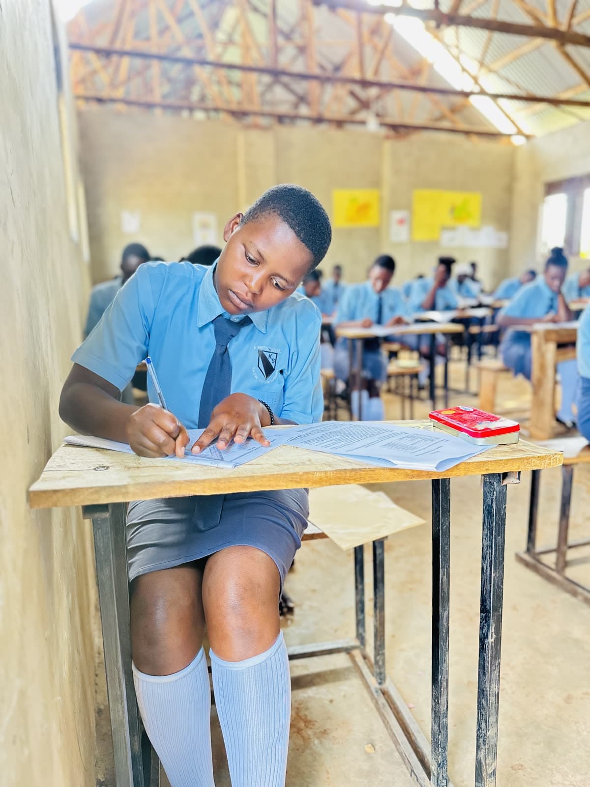 A Ugandan secondary school student writing at her desk during class
